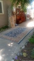 Full view of the area rug laid out lengthwise on a driveway or patio area showing its large size and detailed border and field pattern.