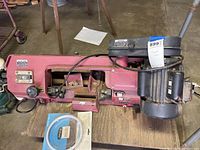 Band saw on wooden board placed on hand truck, showing entire saw and motor assembly from above with garage background.