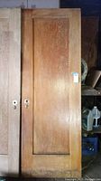 Full view of Douglas Fir wooden door showing natural finish and recessed panel design. Door is propped up in storage area with additional doors visible.
