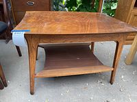 Front view of a wooden mid-century modern coffee table with tapered legs and lower shelf.