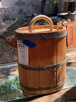 View of wooden jug showing vertical slats, metal bands, handle, and spout outdoors in natural light.