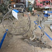 Photo of the wrought-iron circular wine rack and metal book stand placed on floor with background items.