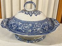 Side view of the covered blue and white serving bowl with floral pattern on lid and base, showing the loop handle on lid.
