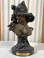 Full view of bronze Salome bust showing headscarf, detailed face and upper torso with sword sheathed at chest, mounted on round black base with a brass plaque.