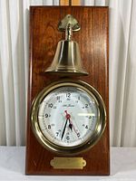 Full view of Seth Thomas clock mounted on wood plaque with brass bell above and inscription plate below.