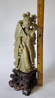 Front and side view of the carved Chinese deity holding a fan, next to a ruler showing about 7 inches tall on a dark wood base.