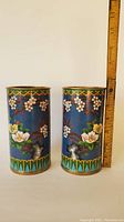 Front view of the two cylindrical cloisonne brush holders with floral patterns and blue enamel background. A measuring ruler shows height approximately 7 inches.