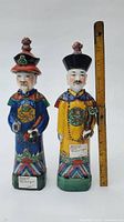 Front view of the two porcelain figurines standing side by side with a ruler showing height approximately 13 inches