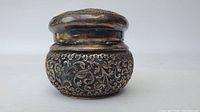 Side angle photo of small silver box showing detailed engraved floral and vine patterns with patina and fitted lid.
