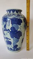 Front view of porcelain vase with blue grape and vine decoration and ruler showing height approximately 10 inches.