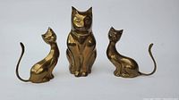 Trio of brass cat figurines arranged in sitting position, with two smaller cats flanking a larger cat.