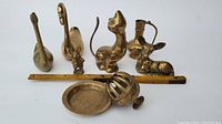 Photo showing all brass figurines including swan, deer, cat, angel, plate, pitcher, and floral-shaped object along with a measuring ruler for scale.