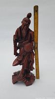 Front view of Chinese hardwood carving of bearded man holding a staff next to a ruler for scale, height about 11 inches