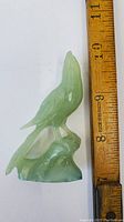 Frontal view of the pale green jade bird carving next to a ruler for size reference showing approximately 3.5 inches tall.