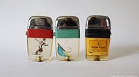 Front view of three collectible vintage lighters with clear bases showing a baseball player, fish hook, and Yellow Pages logo