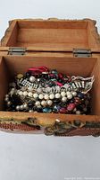 Open carved wooden box showing assorted necklaces and bracelet inside.