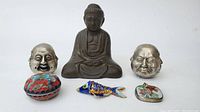 Overview of all items: seated Buddha statue, two metal Buddha heads, round cloisonné trinket dish, cloisonné fish pendant, and floral cloisonné pendant.