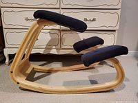 Side view of wooden kneeling chair showing curved frame and blue padded seat and knee pads