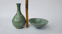 Green Korean vase with crane motif next to a measuring stick showing approx. 7 inches height and matching green dish with black pattern inside