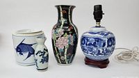 Four porcelain items displayed: white fish pot, small blue floral bottle, black floral vase, and blue and white lamp base with wooden stand.