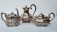 Front view of three silverplate tea and coffee pots showing shapes and design details.
