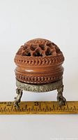 Front view of nutshell shaped wooden incense burner with perforated top and decorative metal stand base on ruler for scale.