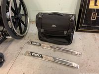 Samsonite travel bag with two packaged Trico Viper wiper blades on the ground next to a wheelchair.