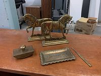 Overview of all brass items including two horse figurine bookends, rocker blotter, letter opener, and decorative tray.