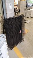 Folded black metal Kong dog crate leaning against a wall, showing the crate folded flat for storage or transport.