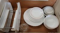 Box containing various plates, bowls, a glass sugar bowl with lid, and a white two-tier metal rack.