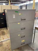 Front view of gray metal four drawer filing cabinet showing scuffed surfaces and recessed handles on each drawer.