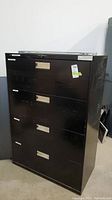 Black metal filing cabinet with four drawers, visible scratches, taped lock, and no key present.