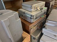 Stack of three metal cases and one brown leather briefcase, showing sizes and condition.