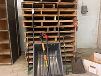 Full view of the three garden tools showing a large grey plastic snow shovel, a green planting/weeding tool, and a metal shovel with red handle.