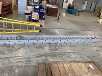 Side view of the full extended ladder lying flat, showing aluminum rungs and structure on warehouse floor.