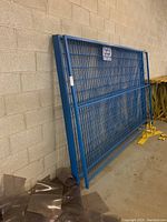Four blue metal fence panels leaning against a concrete block wall