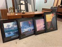 Four black framed inspirational prints leaning against a table, showing varied nature and action images with motivational quotes.