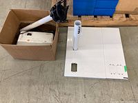 Epson projector and stand base displayed on floor; projector and stand stored inside a box