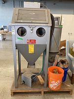 Front view of sandblast cabinet on stand, dust collector and buckets on pallet
