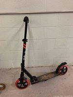 Photo of the scooter showing side profile, displaying black frame, red and black wheels, deck with LaScoota logo, and folding mechanism.