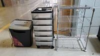 Photo showing metal shelving, plastic drawer organizer, and Staples shredder side by side on floor
