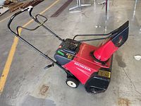 Side view of red Honda snow blower showing handle, auger housing, wheels