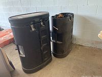 Photo showing two black plastic trade booth display containers side by side against a wall on a concrete floor.