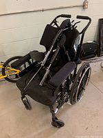 Wheelchair folded partially showing padded armrests, backrest, large rear wheels, front casters, and various support cushions.