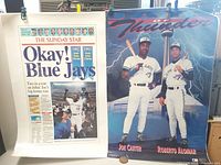 Two laminated Blue Jays posters clipped and displayed, one with a newspaper headline and a Jays of Thunder poster with players Joe Carter and Roberto Alomar.