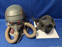 Two masks side by side: Killzone video game helmet mounted on plaque with hoses and black rubber gas mask.