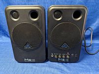 Front view of pair of black Behringer MS16 active monitor speakers, one with controls and both with speaker grilles and logo.