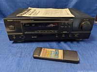 Front view of Denon DRA-375RD stereo receiver powered on, showing digital display tuned to FM 87.50 MHz, with remote control and manual on top and in front.