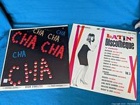 Two vinyl LPs: Latin Discotheque Vol. 5 with a woman in black dress on cover and a Cha Cha Cha album with black cover and colored letter disco design.