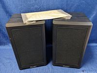 Pair of Mission 760i bookshelf speakers with black fabric grilles, wood grain finish on top and sides, black frame around front.